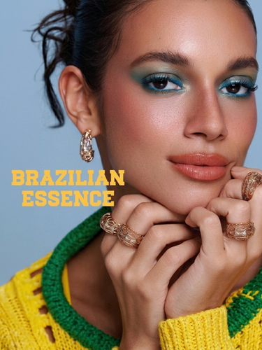 Model wears blue eye makeup, terracotta lipstick, and three intricate gold cage-style rings.