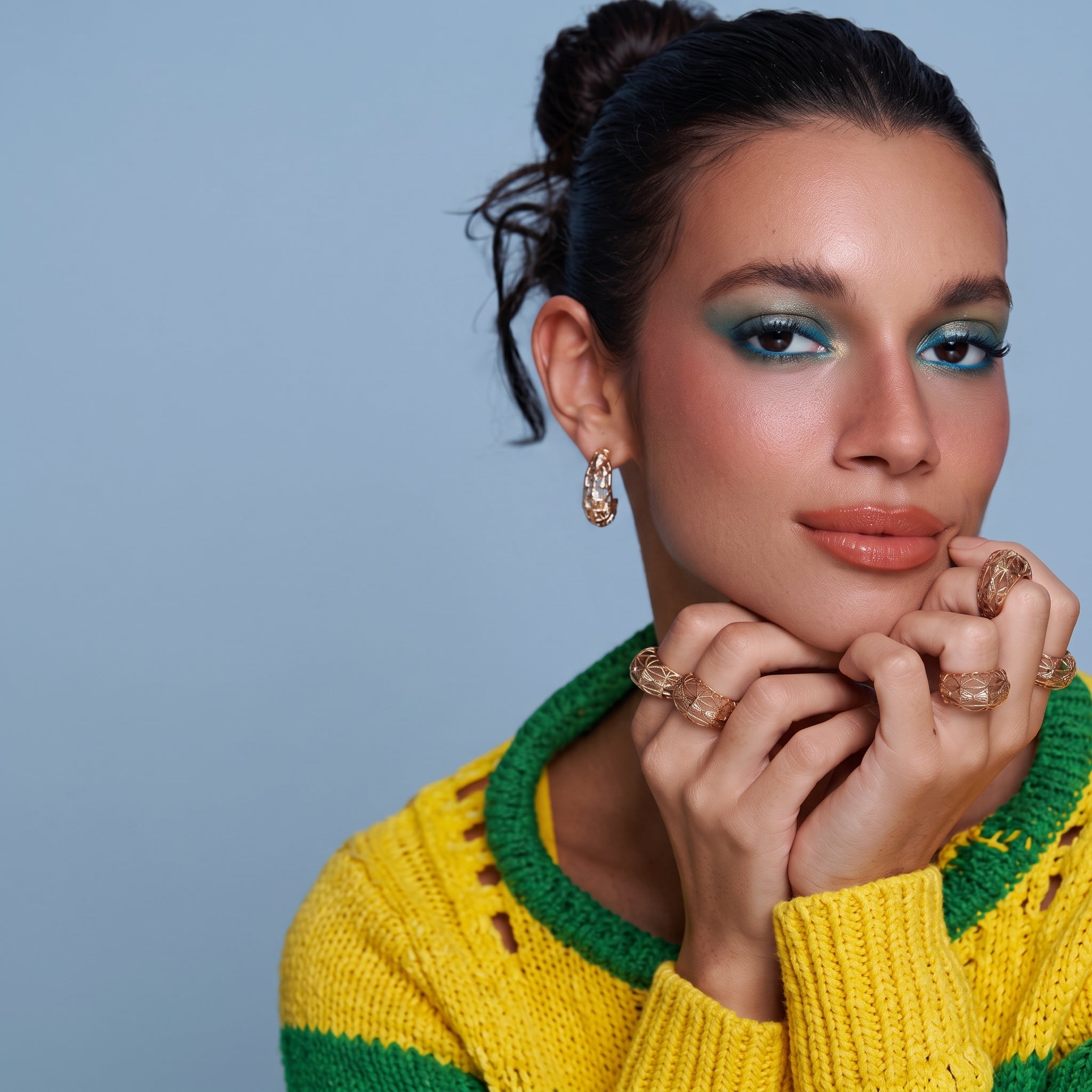 Model wearing gold jewelry featuring abstract, cut-out designs. Includes an oval hoop earring and multiple rings on fingers.