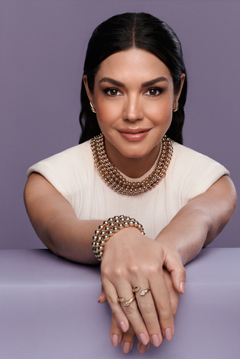 Woman wearing a chunky gold beaded choker necklace, matching bracelet, small hoop earrings, and open gold rings.