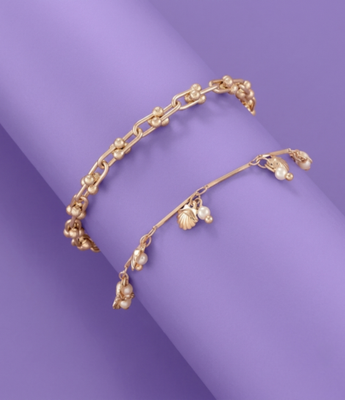 Stack of two gold bracelets: a gauge link chain and a charm chain with pearls and seashells.