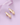 Product photo on a soft lavender background featuring a pair of smooth, polished gold stud earrings with an organic curved teardrop shape, positioned beside a folded purple satin ribbon.