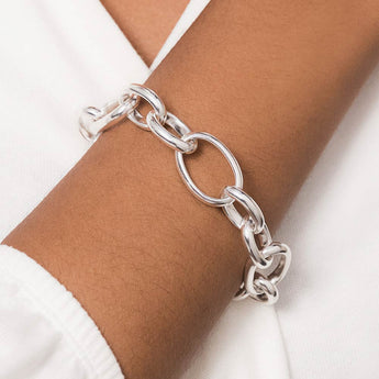 A chunky silver chain bracelet featuring shiny interconnected oval links on a dark-skinned arm with a white sleeve