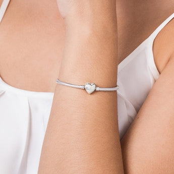 Photograph of a Rommanel silver-toned snake chain bracelet on a woman's wrist featuring a polished heart-shaped clasp with brand engraving and a white sleeveless blouse