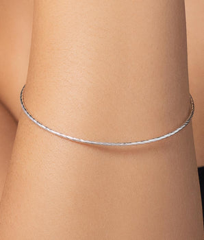 Photograph of a slender silver bracelet on a person's wrist featuring a delicate twisted texture and a minimalist profile with a high-polish finish