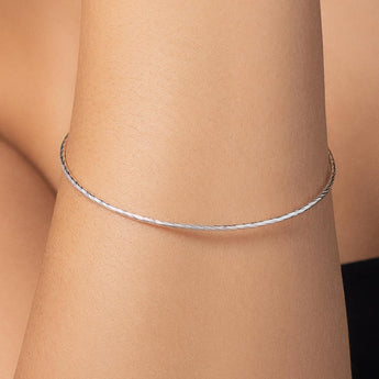 Photograph of a slender silver bracelet on a person's wrist featuring a delicate twisted texture and a minimalist profile with a high-polish finish