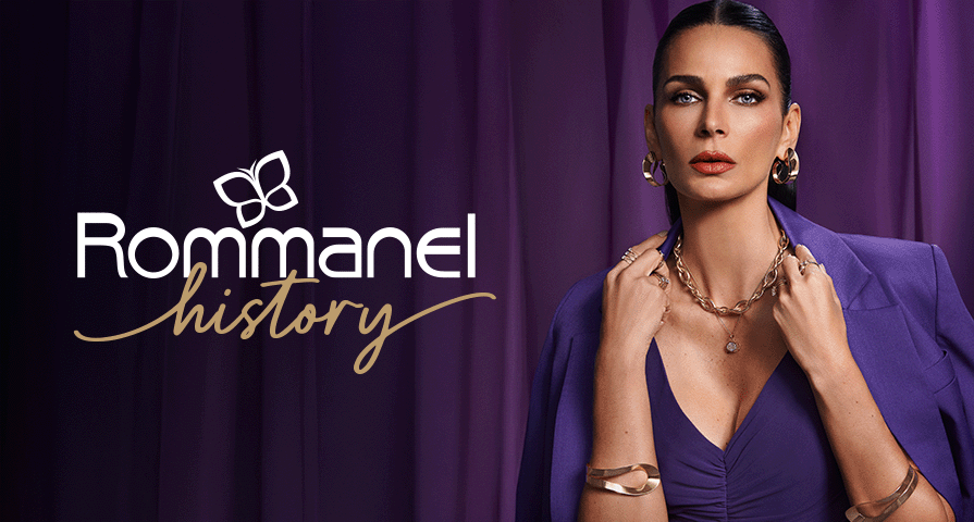 Promotional image with the Rommanel History logo on a purple curtain background, featuring a woman in a purple blazer wearing a bold gold link chain necklace, hoop earrings, and gold cuffs.