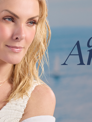 A blonde model poses against a serene ocean background while holding a rope, showcasing a gold fashion jewelry collection with deep blue teardrop gemstones—including layered necklaces, matching earrings, and a statement ring. Navy text on the right reads "azure Amore" followed by "Ana Hickmann Fashion Jewelry."