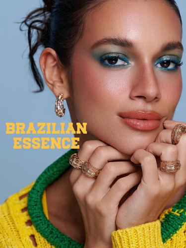 Model wears blue eye makeup, terracotta lipstick, and three intricate gold cage-style rings.